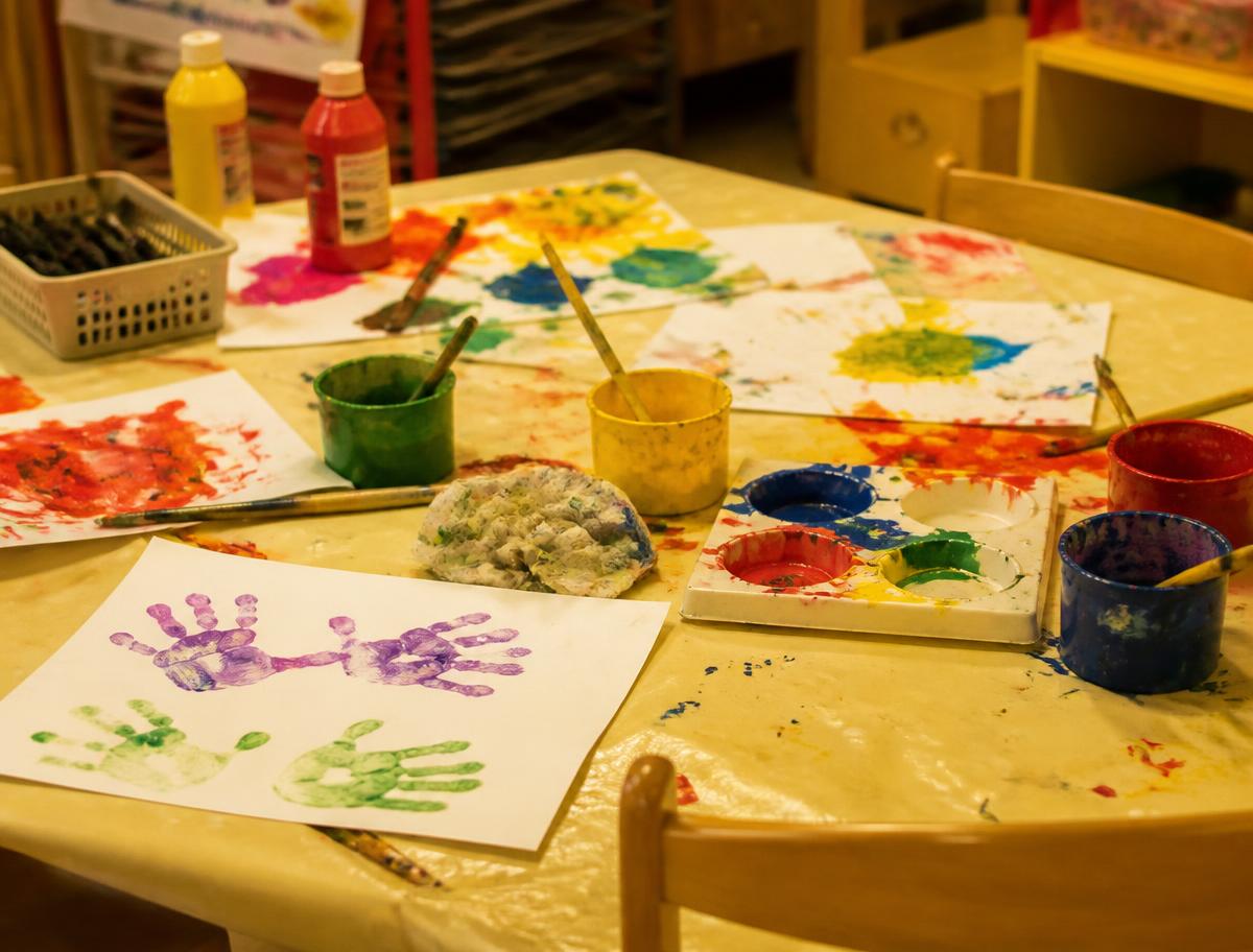 Messy art table covered in paint pots and children's handprints